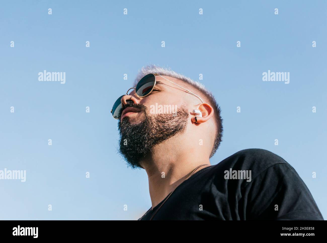 From below of calm male with black beard and mustache in sunglasses and  casual clothes looking away against cloudless blue sky in sunlight Stock  Photo - Alamy