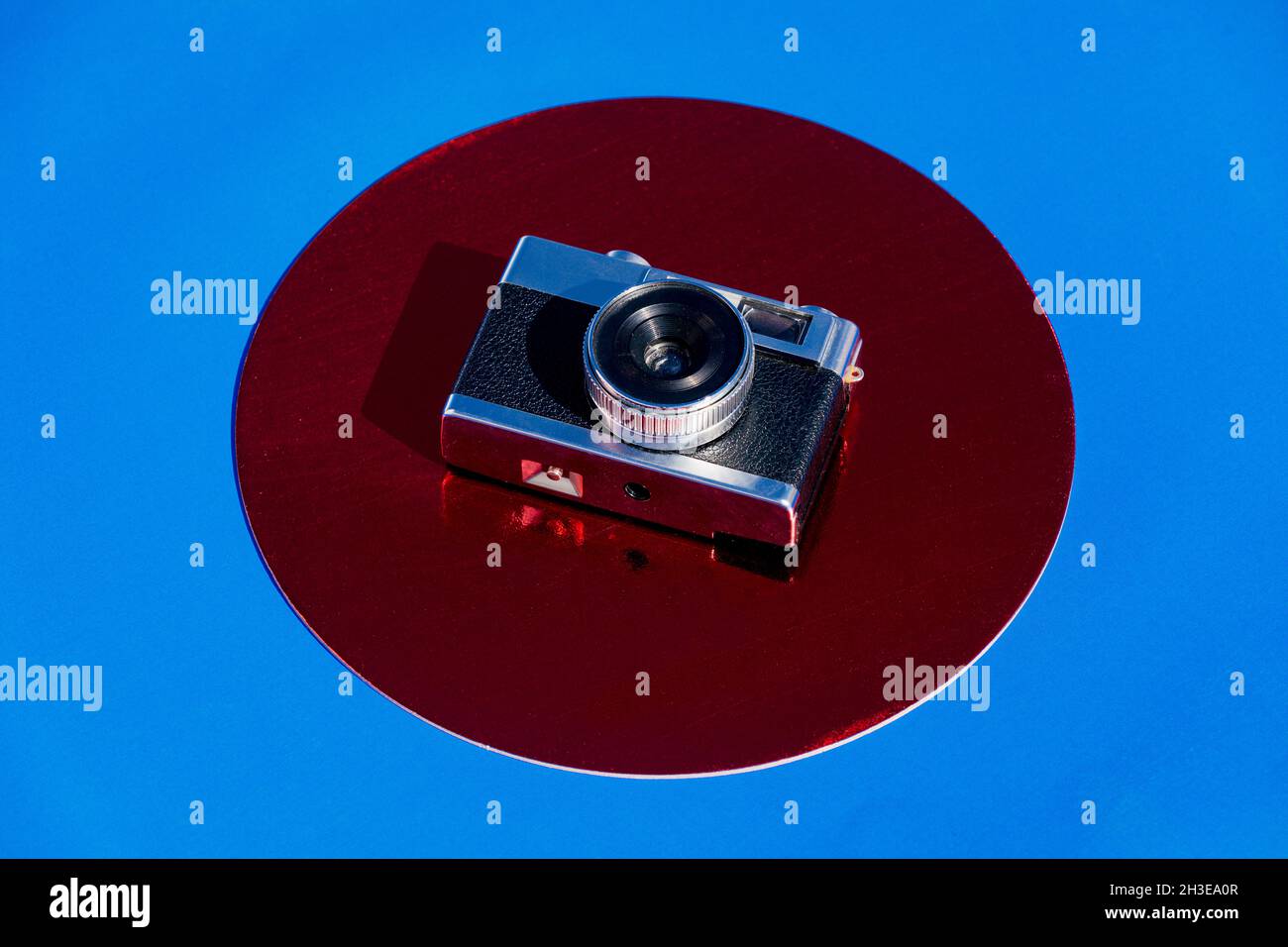 From above retro photo camera placed on metallic red circle on blue background Stock Photo