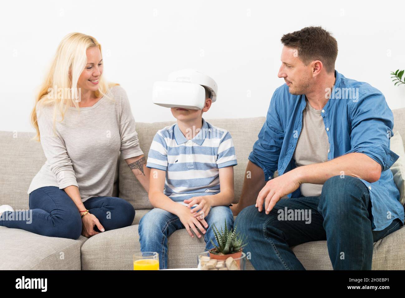 Happy family at home on living room sofa having fun playing games using virtual reality headset Stock Photo