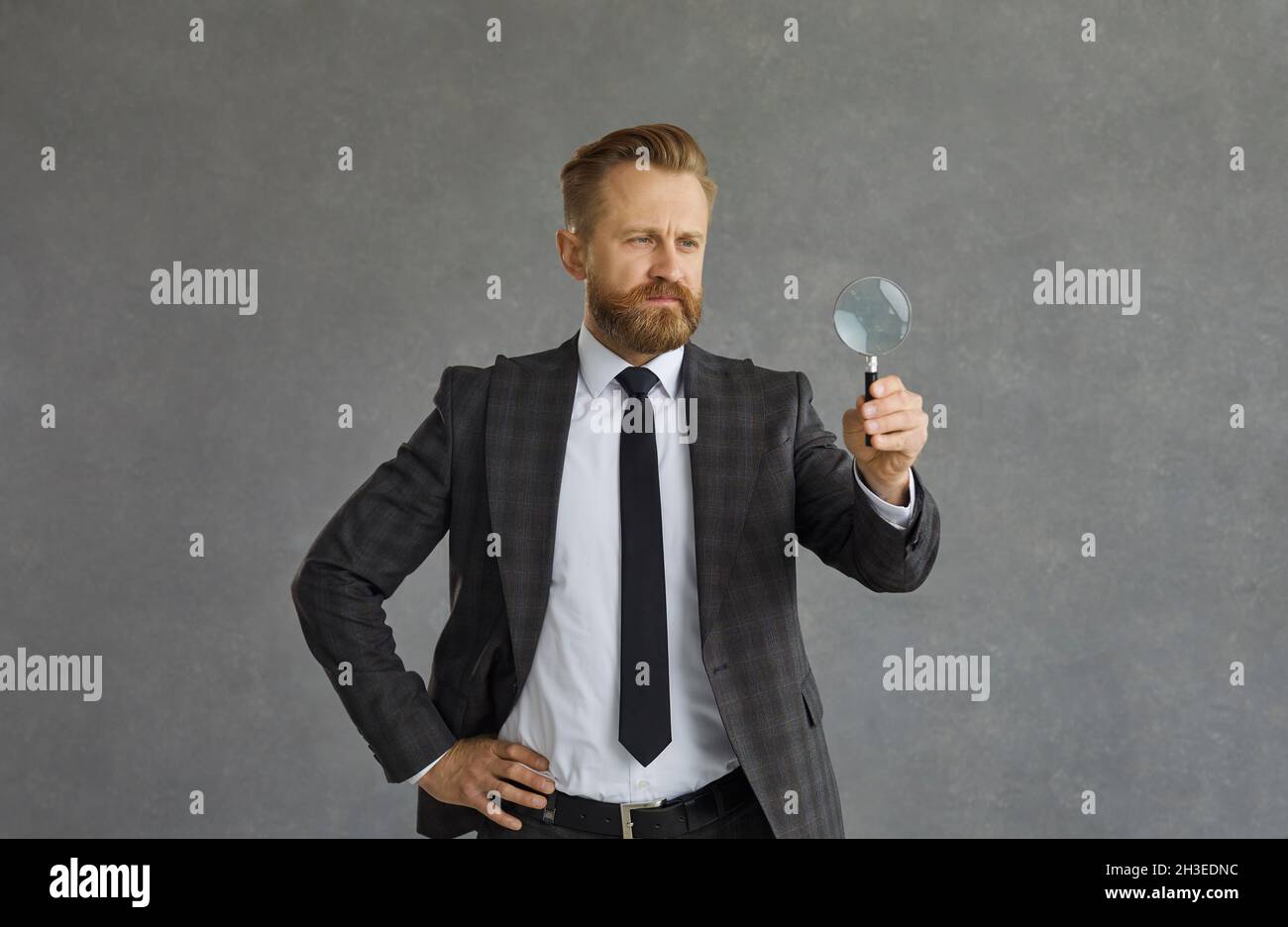 Studio portrait shot of concentrated businessman in suit with magnifier Stock Photo