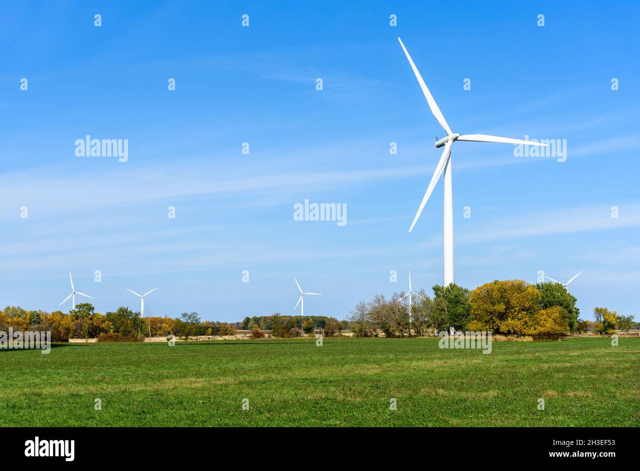 Wind turbine at the far end of a grassy field on a clear autumn day. Other wind turbines are visible in background. Copy space. Stock Photo
