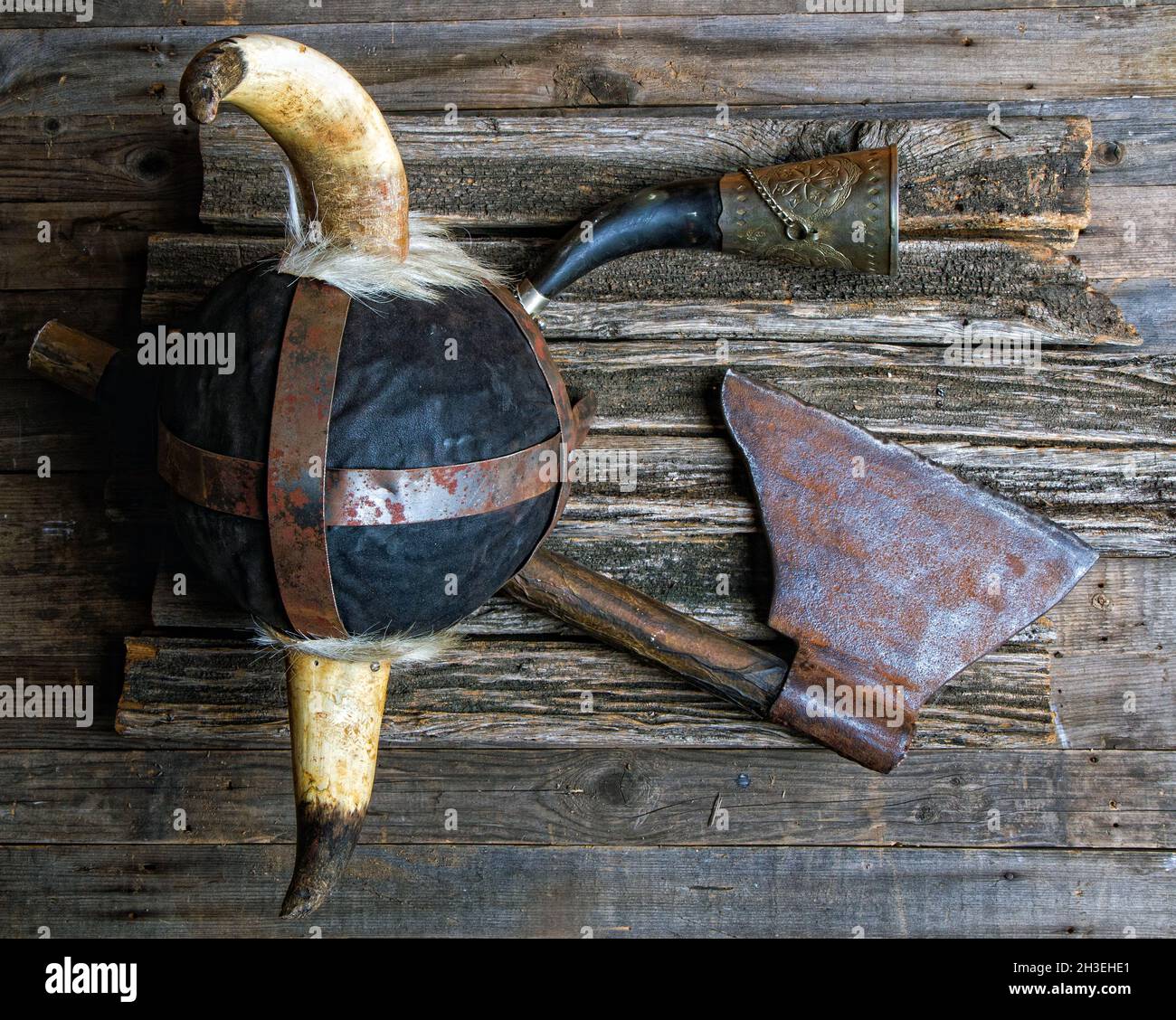 battle ax horned helmet and viking signal horn on rough wooden table top view Stock Photo