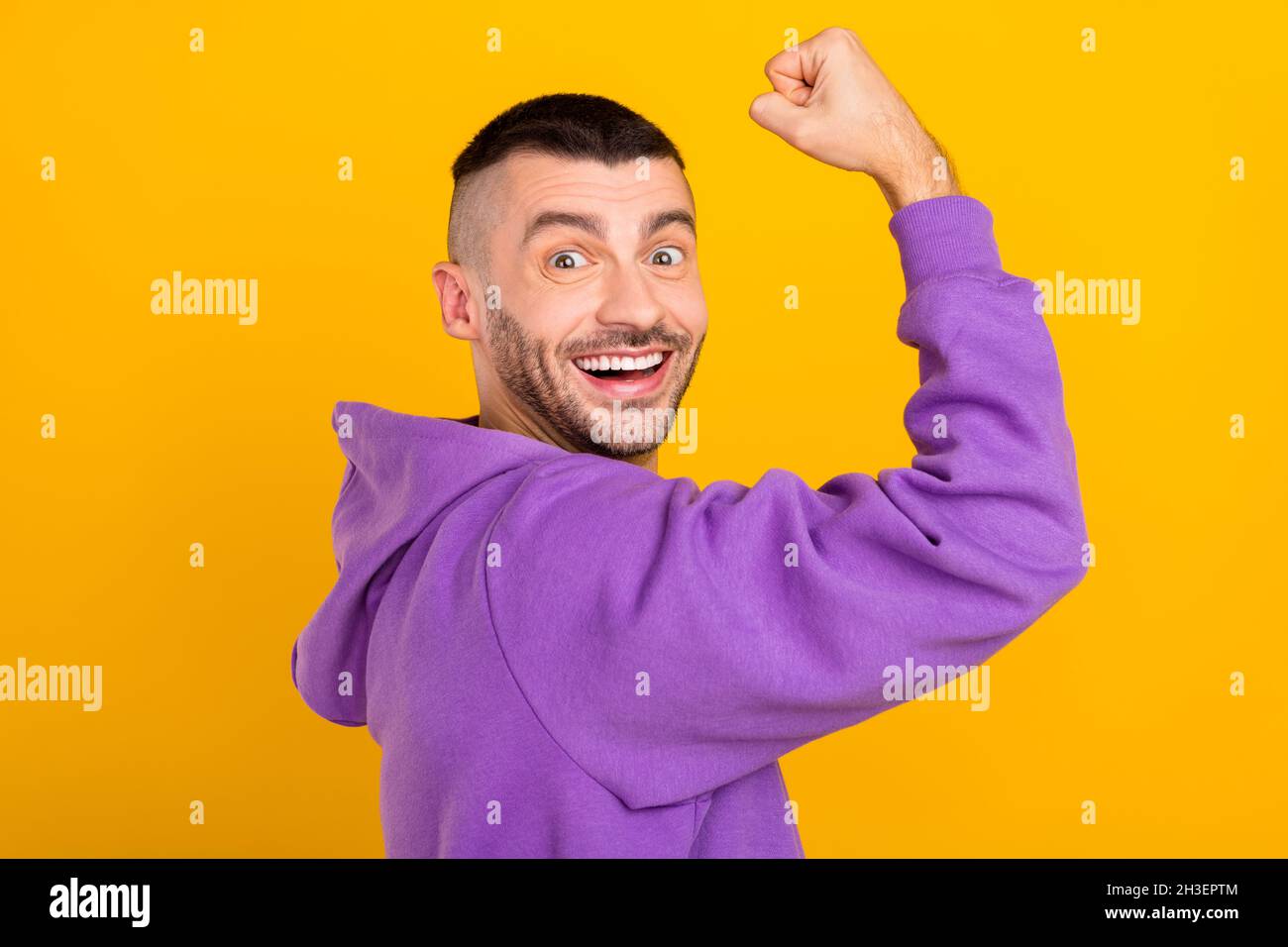 Photo portrait young man wearing purple hoody showing strong biceps isolated vivid yellow color background Stock Photo