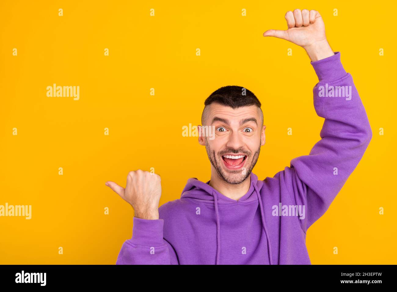 Photo portrait young man wearing purple hoody showing copyspace with thumb isolated vivid yellow color background Stock Photo