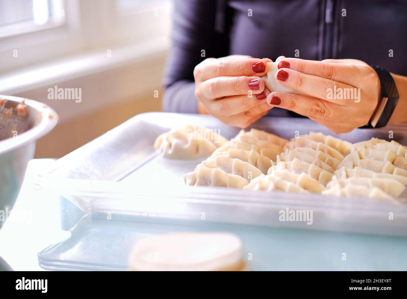 Beautiful lady hands making meat dumpling on table near window at home kitchen. Stock Photo