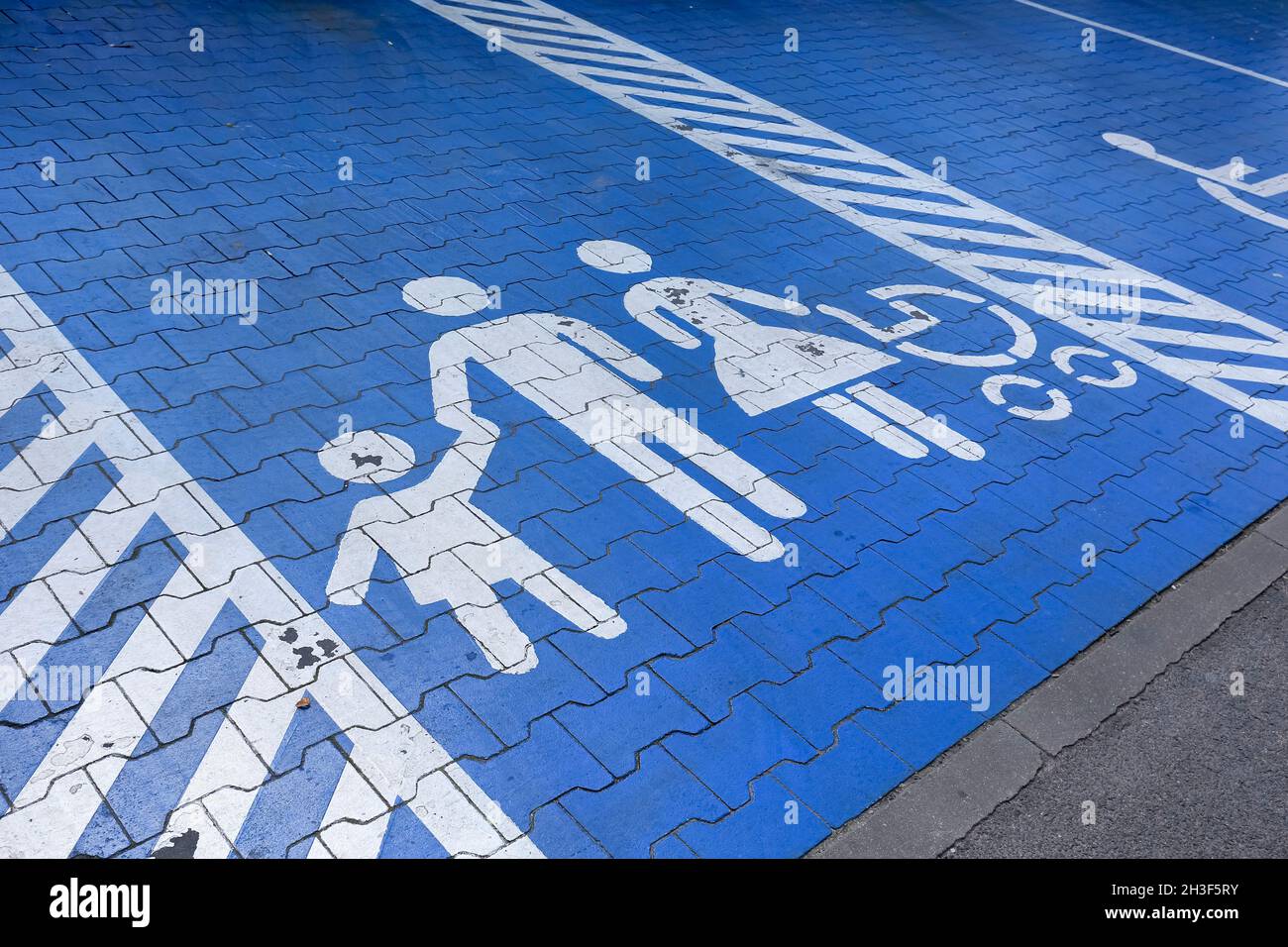 Pictogram showing parents with kids has been painted white on a blue surface. The sign indicate a parking place reserved only for parents with kids. Stock Photo