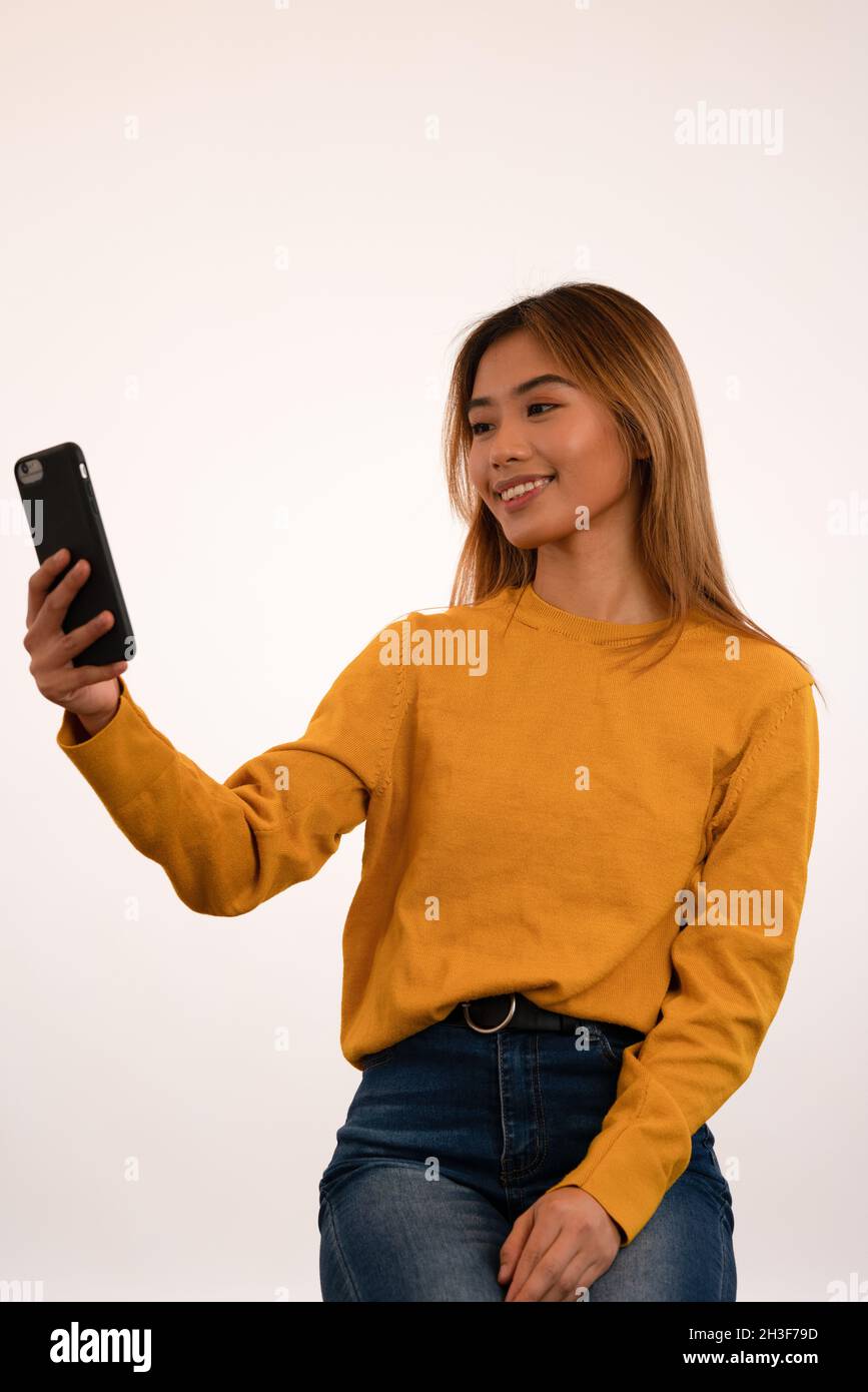Young attractive asian girl smiling while using smartphone in studio Stock Photo
