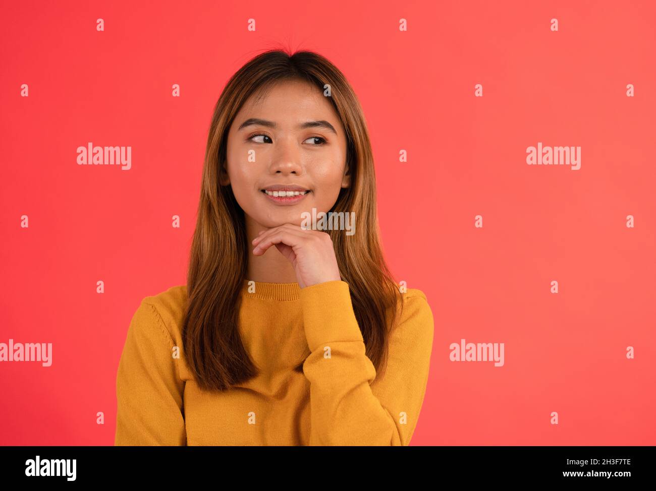 Portrait of young attractive asian girl smiling while thinking with hands on chin Stock Photo