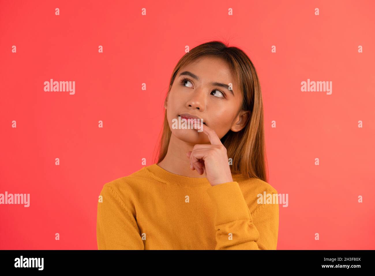 Portrait of young attractive asian girl smiling while thinking with hands on chin Stock Photo