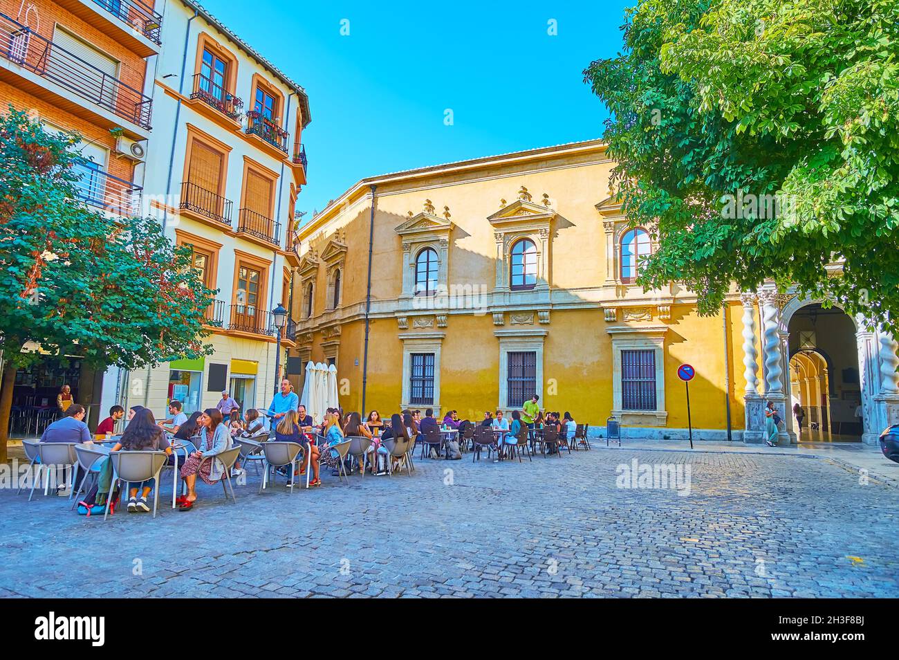 GRANADA, SPAIN - SEPT 27, 2019: University Square with outdoor cafes and historic building of Faculty of Law of Granada University, decorated with Sol Stock Photo