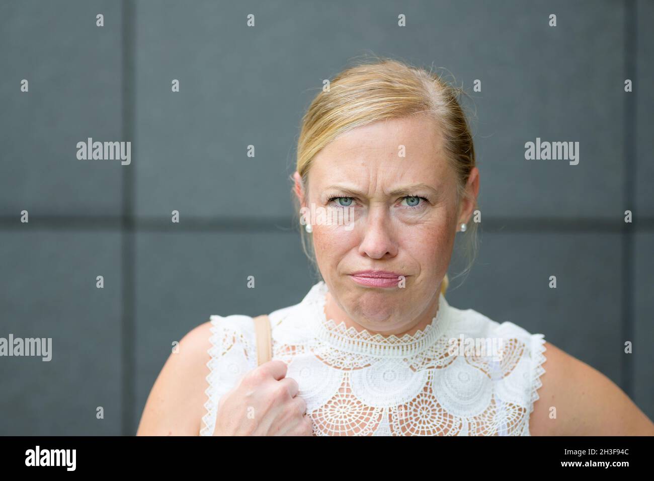 Angry petulant blond woman glaring at the camera with an intense expression against a grey wall in a close up portrait Stock Photo