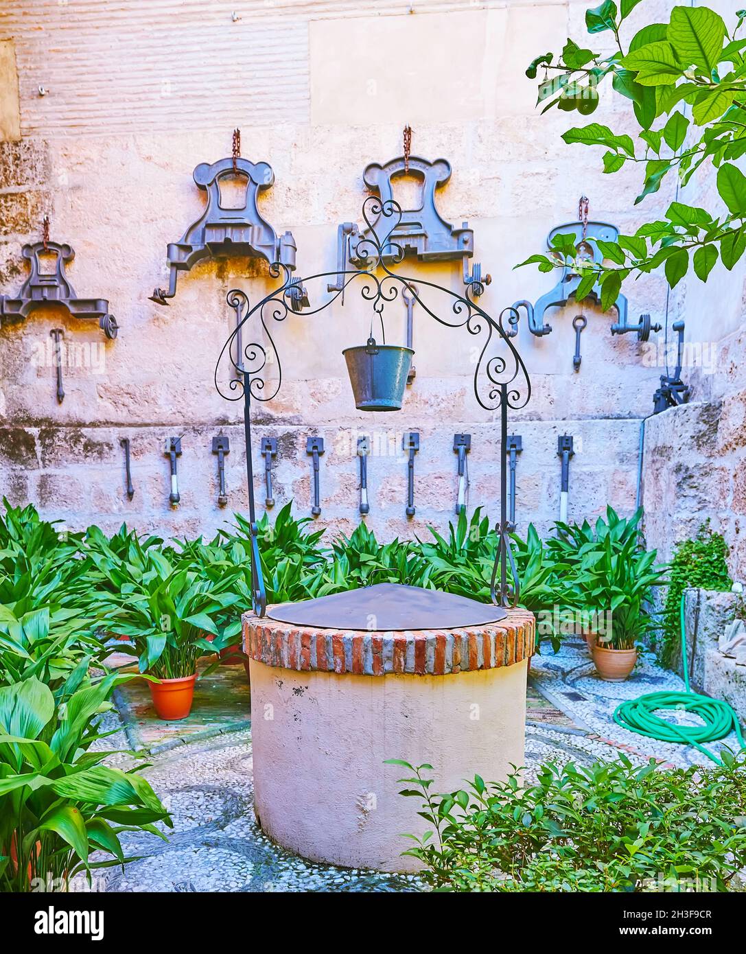 The old well and the small garden with green plants in pots in yard of San Juan de Dios Basilica, Granada, Spain Stock Photo