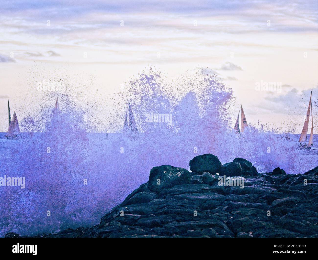 Hawaiian Surf And Sails - Surf crashing against the Magic Island breakwater with a line of sailboats in the background Stock Photo