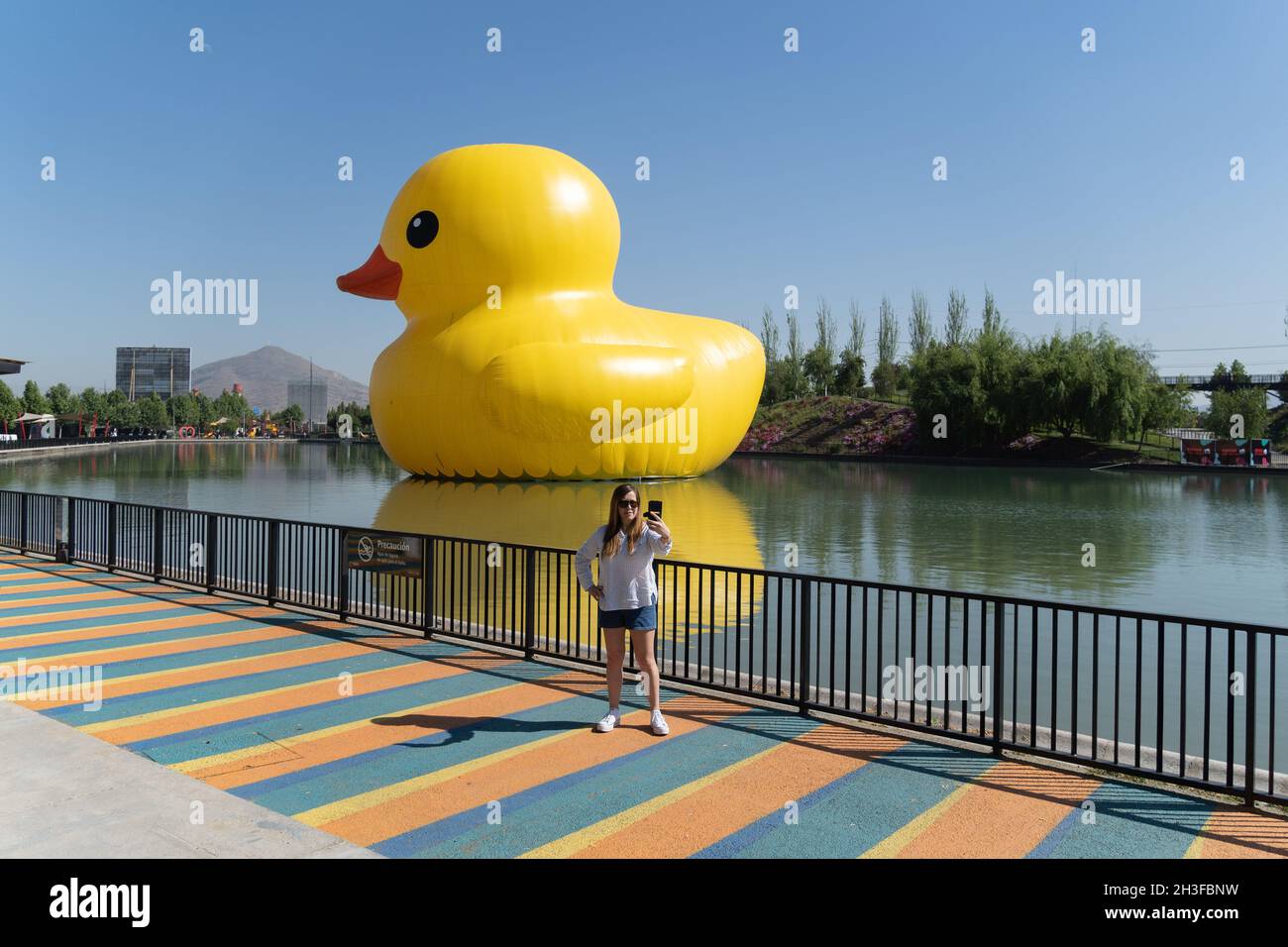 Santiago, Metropolitana, Chile. 28th Oct, 2021. A woman takes a selfie next to a 20-meter high inflatable rubber duck. The duck is part of the Made At Home Fest and is one of the several interventions that were installed in the Parque de la Familia in Santiago, Chile. (Credit Image: © Matias Basualdo/ZUMA Press Wire) Credit: ZUMA Press, Inc./Alamy Live News Stock Photo