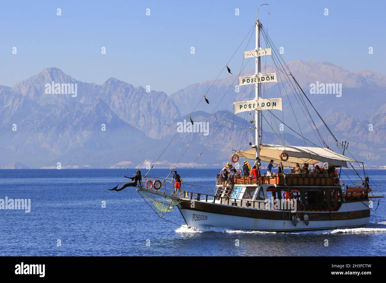 The tourist boat Poseidon is heading southest along the Antalya coast in southern Turkey with a group of tourists. A mermaid figurehead adorns the bow. Stock Photo