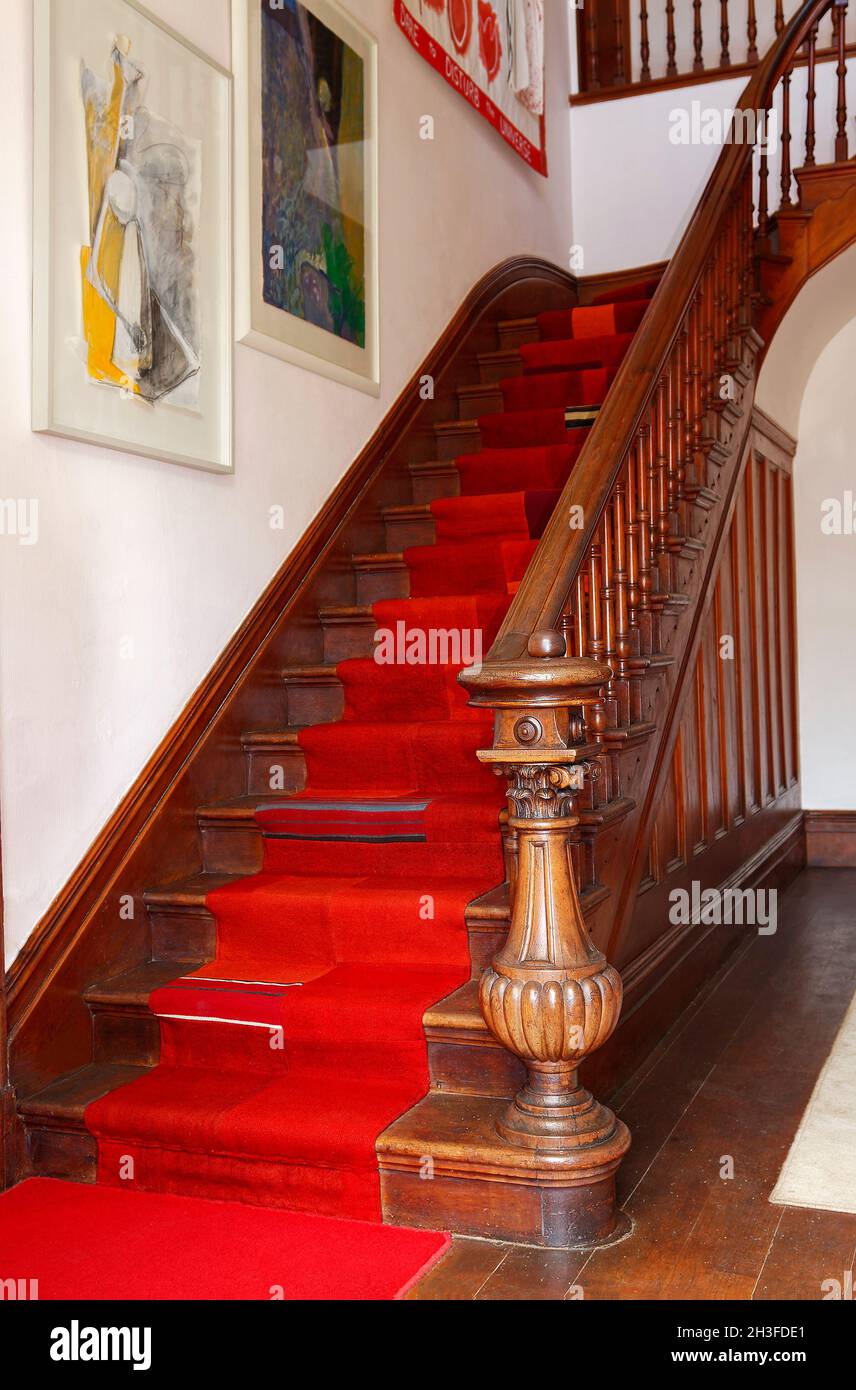 old wood staircase, ornate newel post, pieced red carpet, framed paintings, colorful, attractive, The Giants House, South Island, Akaroa; New Zealand Stock Photo