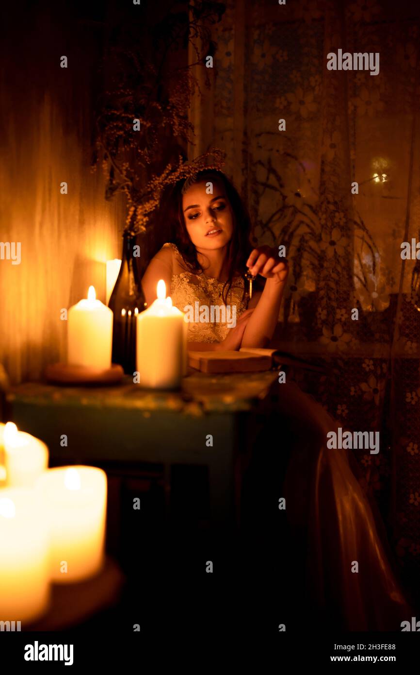 A woman is sitting in a room by candlelight. A young girl looks at burning candles and wonders at her betrothed Stock Photo