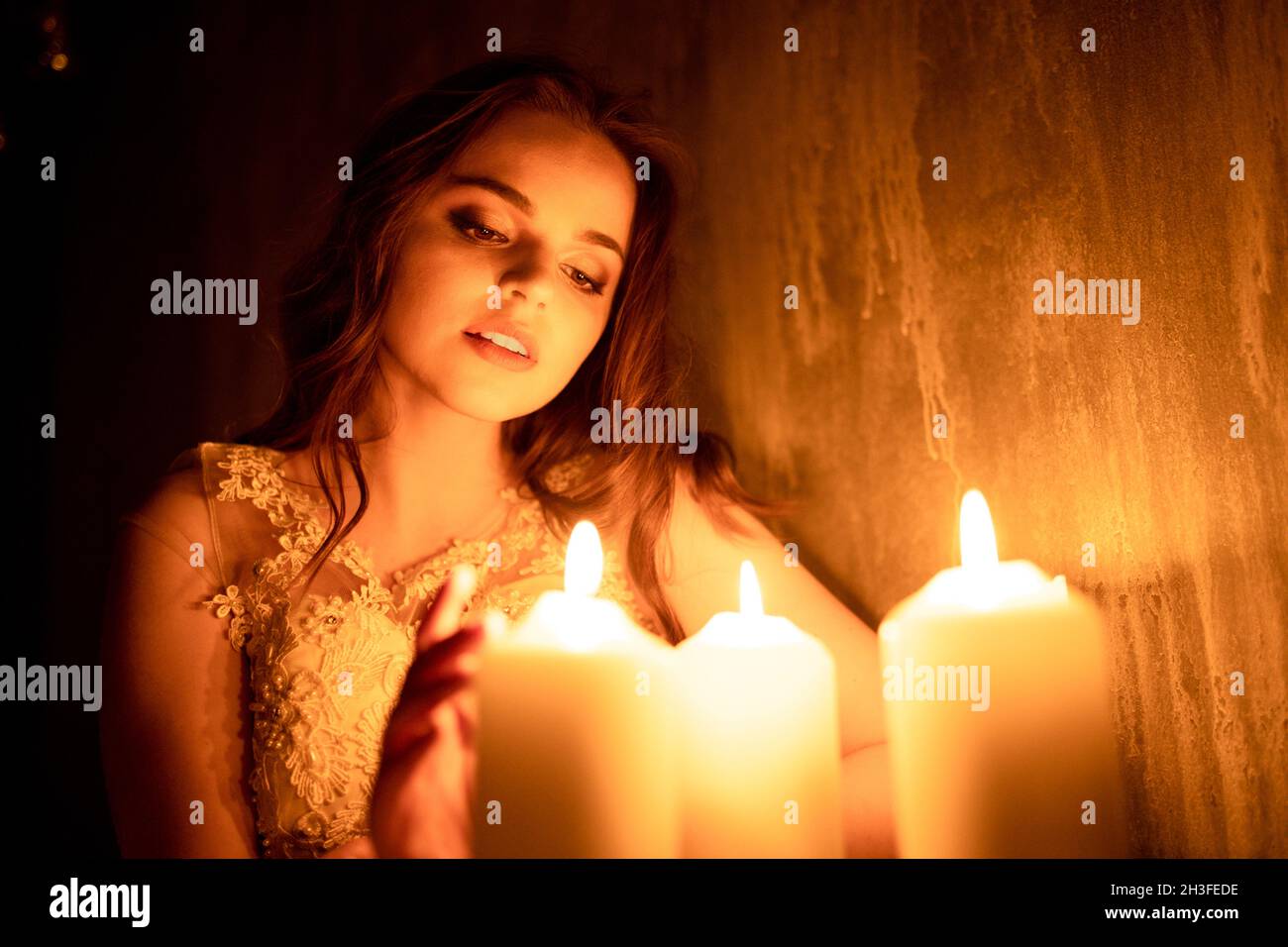 A woman is sitting in a room by candlelight. A young girl looks at burning candles and wonders at her betrothed Stock Photo