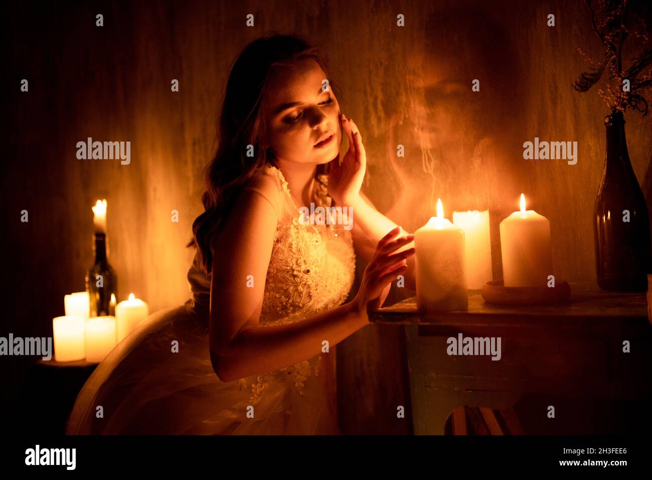 A woman is sitting in a room by candlelight. A young girl looks at burning candles and wonders at her betrothed Stock Photo