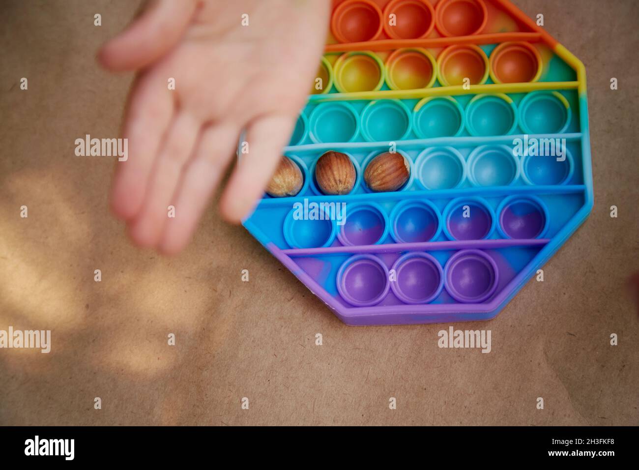 Baby plays with pop it toy and hazel. Game for the development of motor skills. The rainbow touch sensory fidget. Top view. High quality photo Stock Photo
