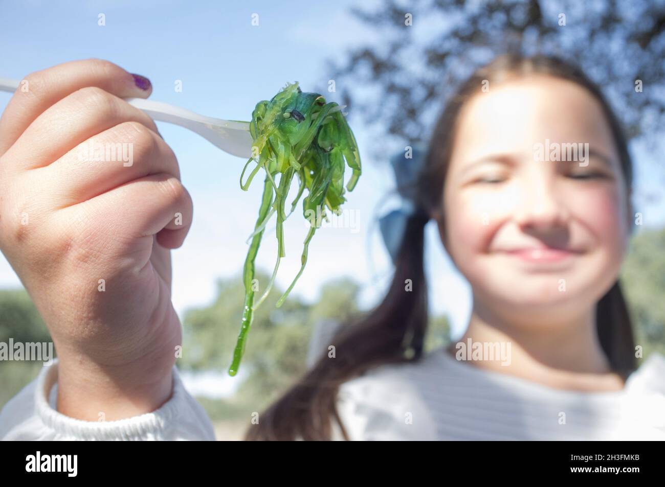 Child girl with wakame salad on fork. Outdoors background Stock Photo