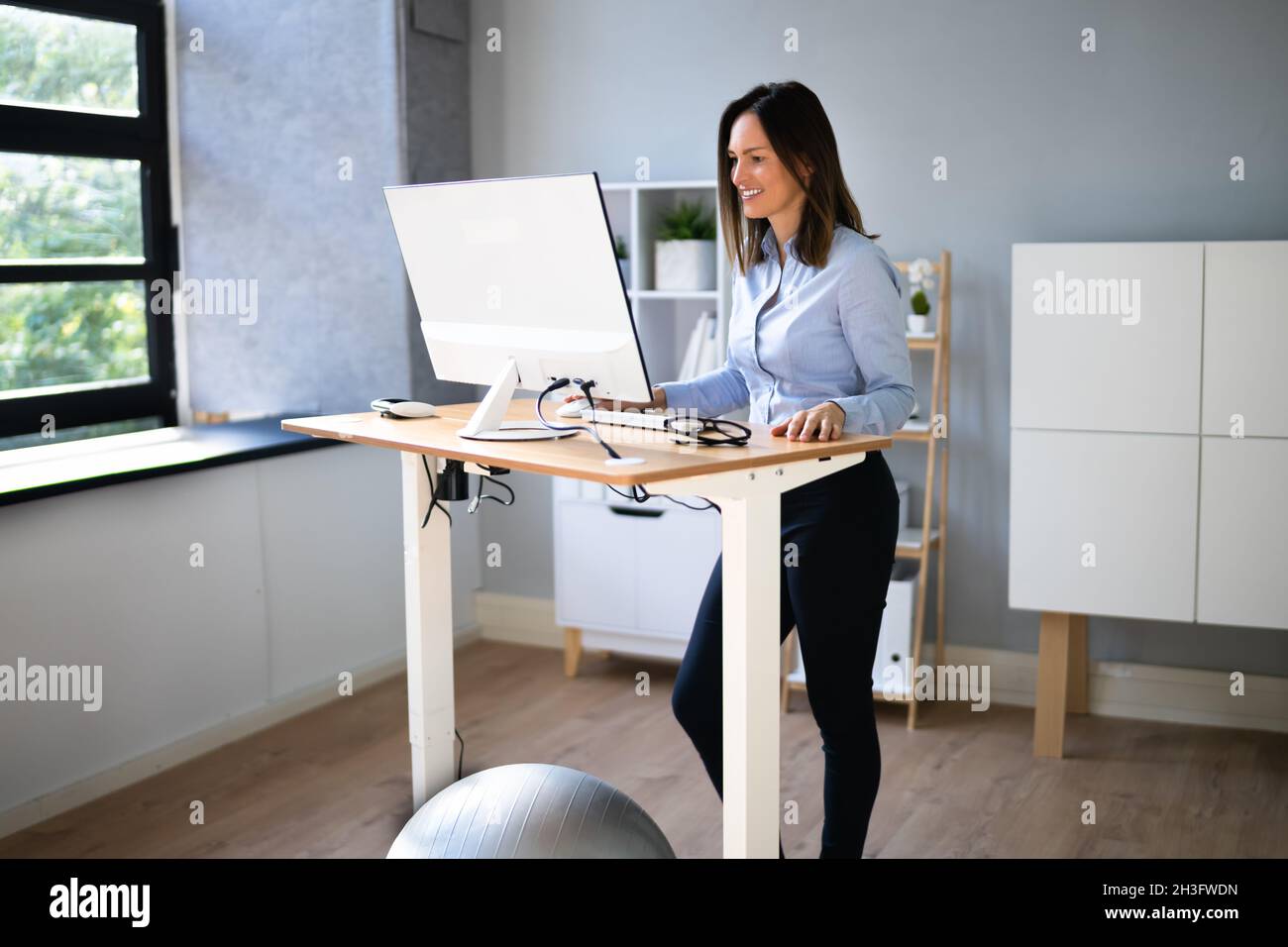 Woman Using Adjustable Height Standing Desk In Office For Good Posture