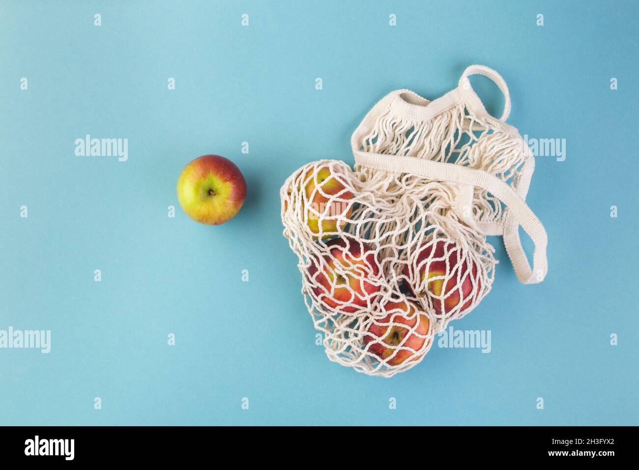 Red apple and string bag on a blue table. Summer or fall season. Eco shopping concept Stock Photo