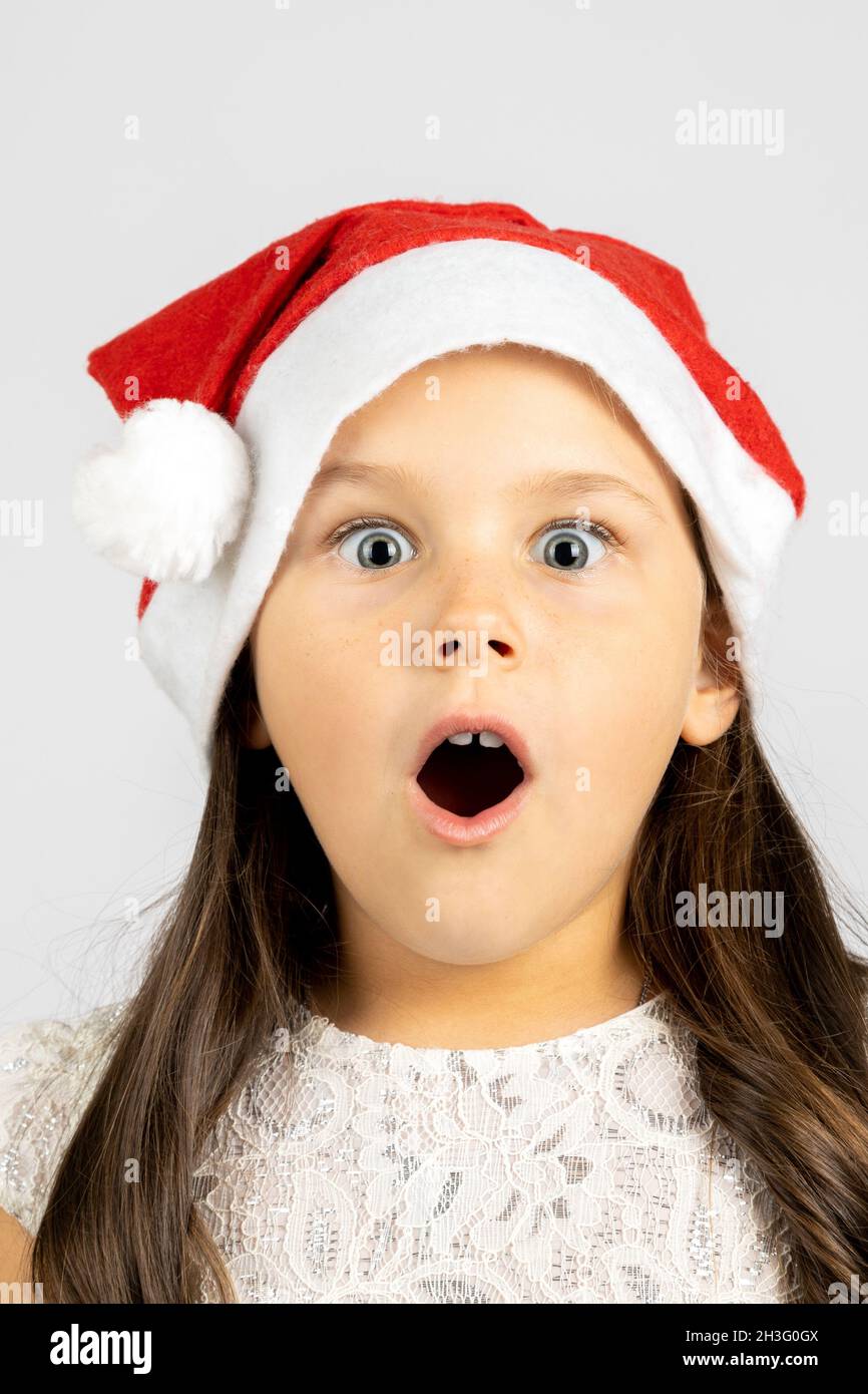 close-up portrait of surprised, shocked, open-mouthed girl in red Santa Claus hat, isolated on white background with copy space Stock Photo