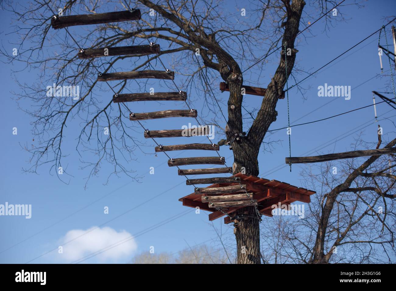 Suspended wooden staircase. ladder in form of bridge is suspended between trees against blue sky, children's attraction in forest Stock Photo