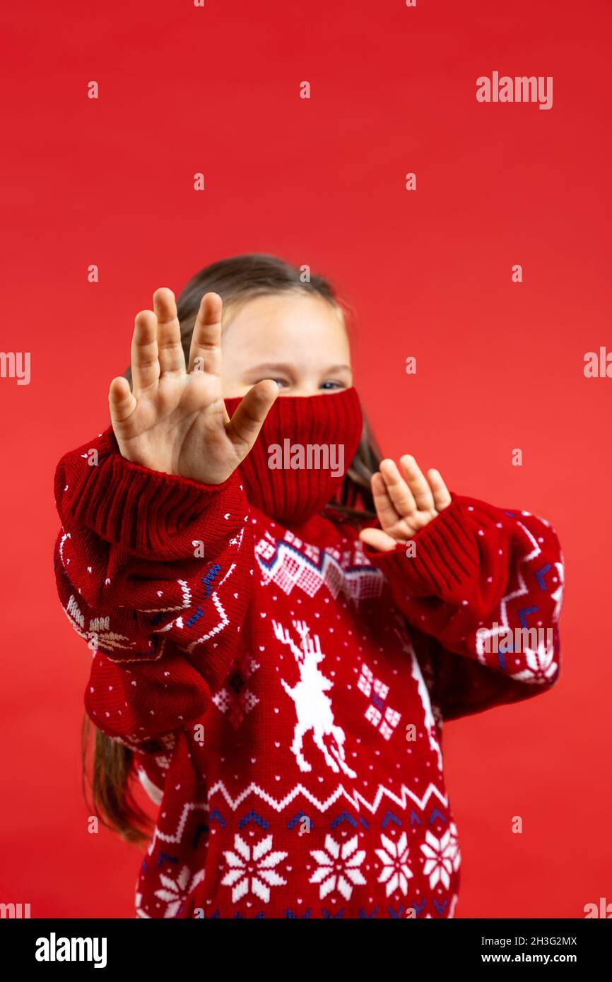 portrait of joyful girl in red Christmas sweater with reindeer and with knitted collar on half face showing palms like ninja , isolated on red Stock Photo