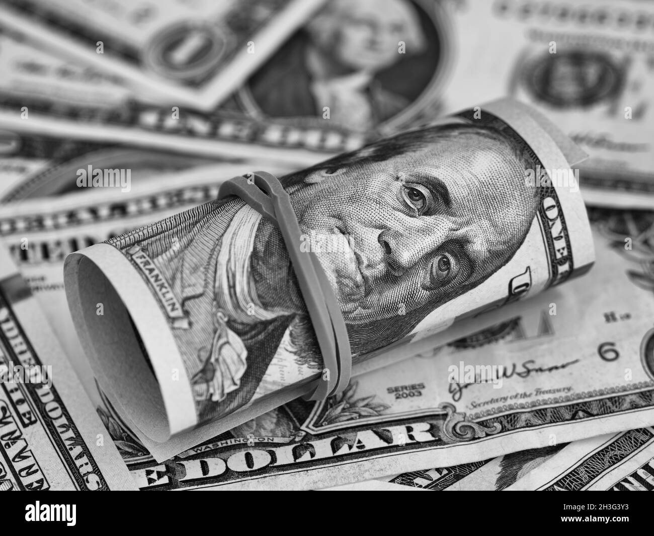 A tied stack of one hundred dollar bills on a dollar bill background. Black and white. Close up Stock Photo