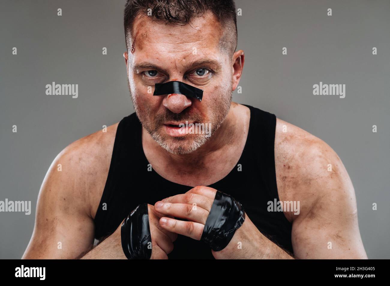 on a gray background stands a battered man in a black T shirt looking like a fighter and preparing for a fight. Stock Photo