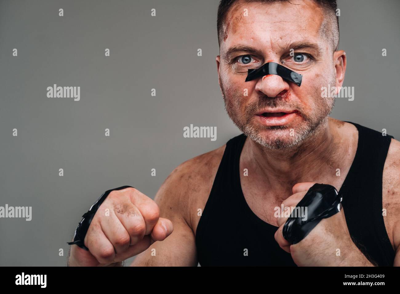 on a gray background stands a battered man in a black T shirt looking like a fighter and preparing for a fight. Stock Photo