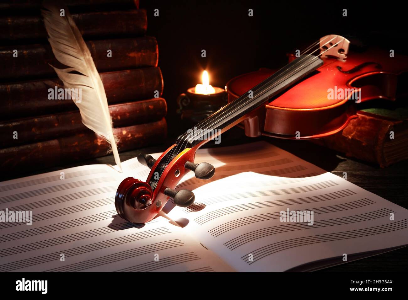 Nice violin near books and feather and candle against black background ...