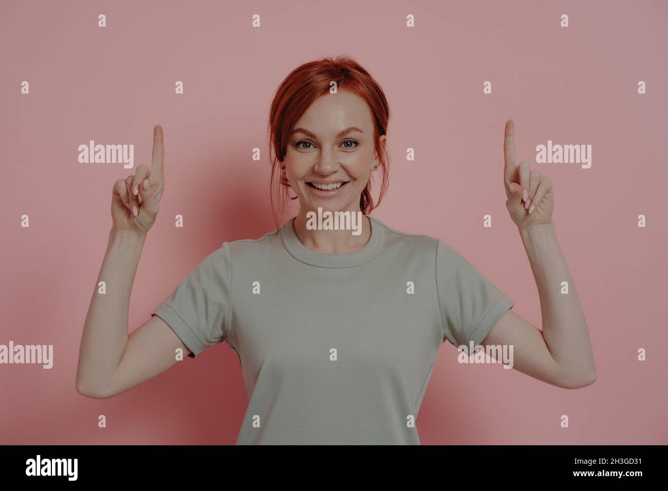 Happy young caucasian woman pointing upwards with index fingers and smiling cheerfully Stock Photo