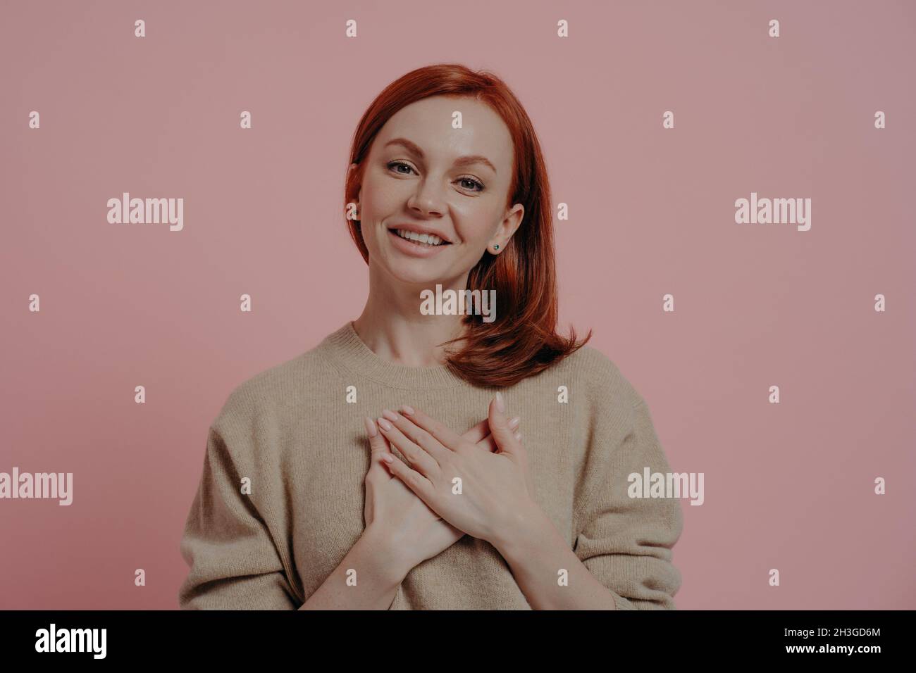 Wishful peaceful young red-haired woman holding hands on chest and thanking, showing gratitude sign Stock Photo