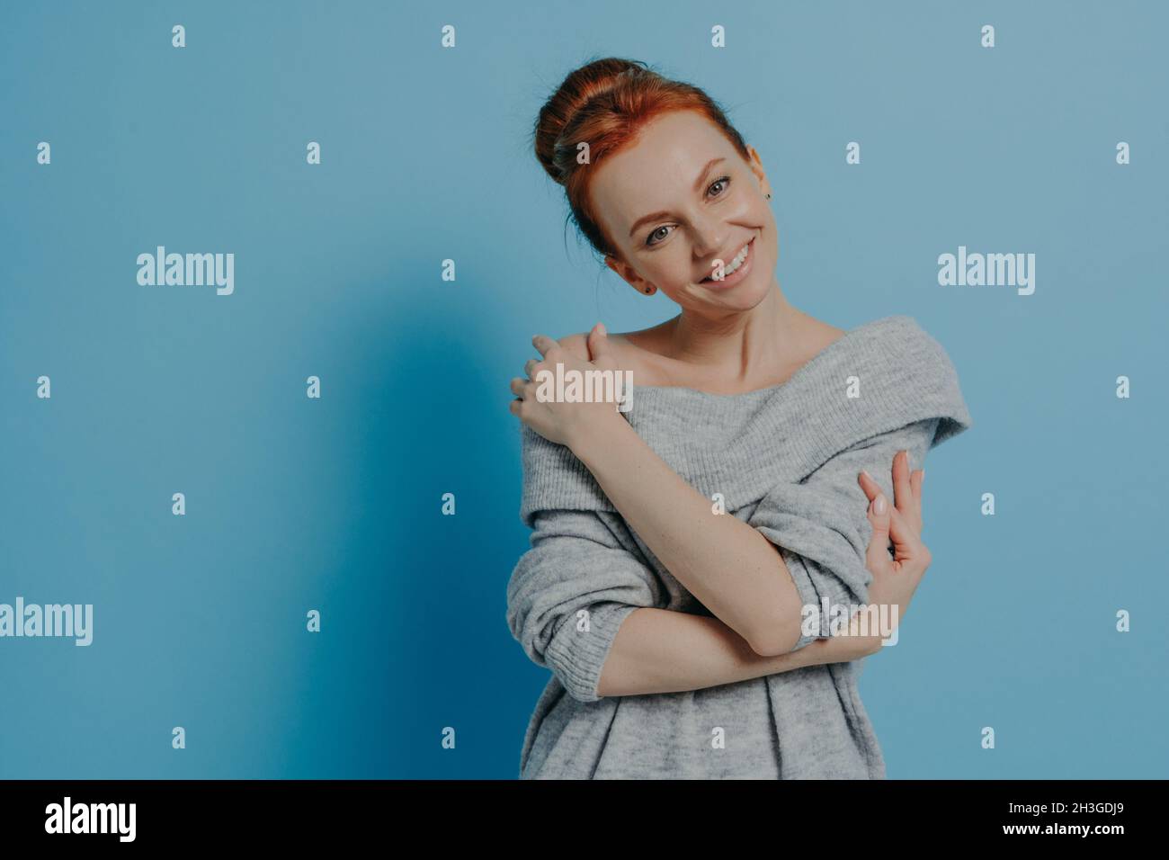 Happy calm ginger female demonstrating self love while posing against blue wall Stock Photo