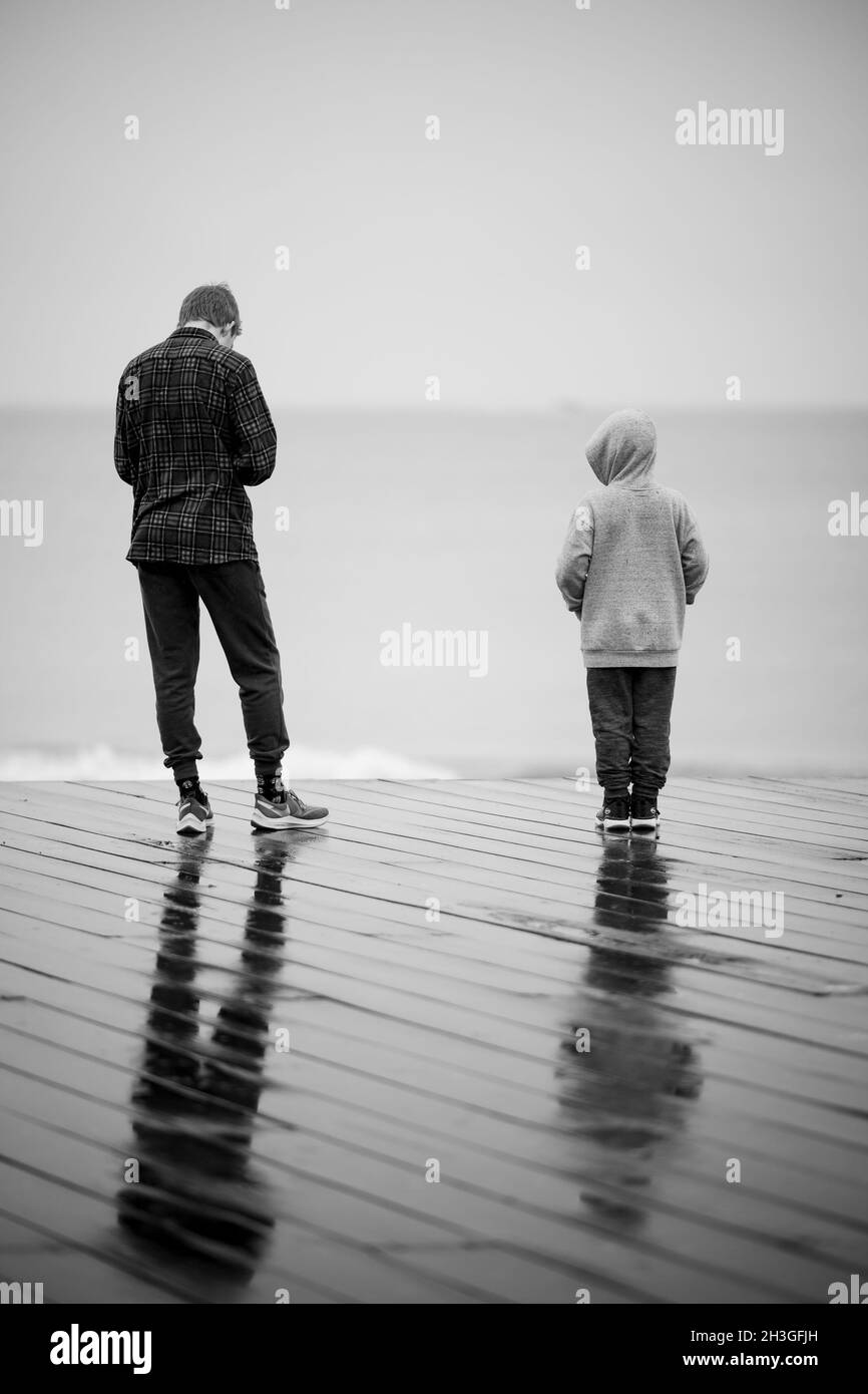 Vertical back view of a father and his child enjoying a rainy day on a pier Stock Photo