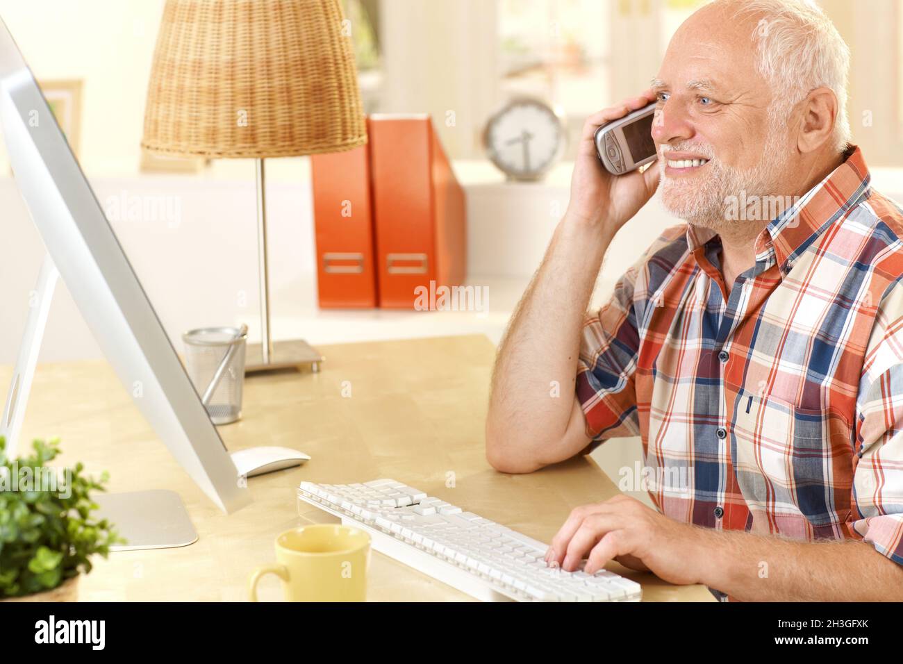 Senior man talking on cellphone, using computer Stock Photo
