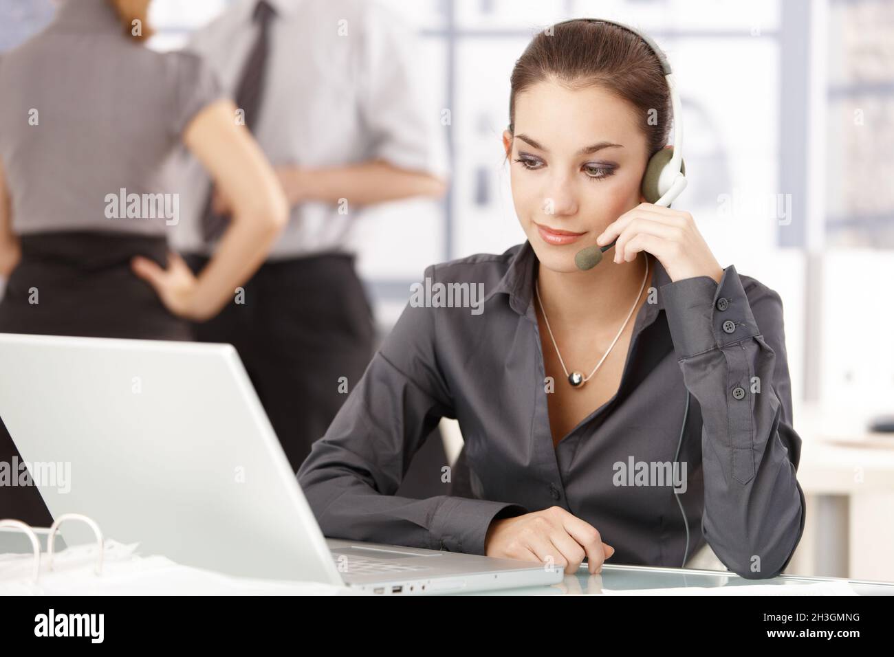 Young office worker using headset sitting at desk Stock Photo