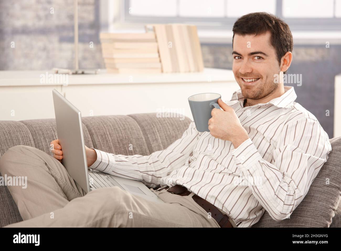 Young man browsing Internet at home smiling Stock Photo