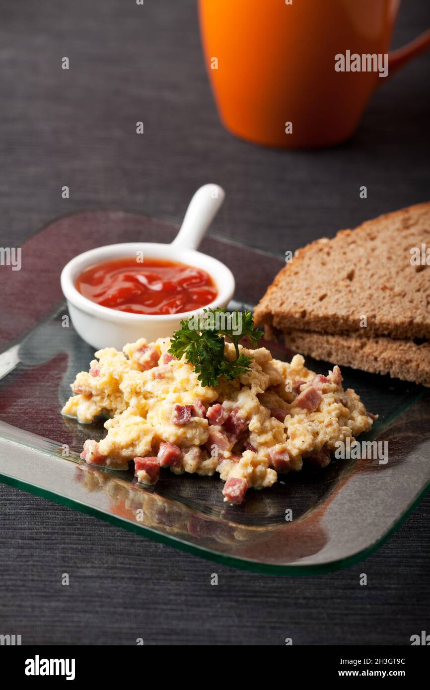 Scrambled eggs with ham cubes on a glass plate Stock Photo