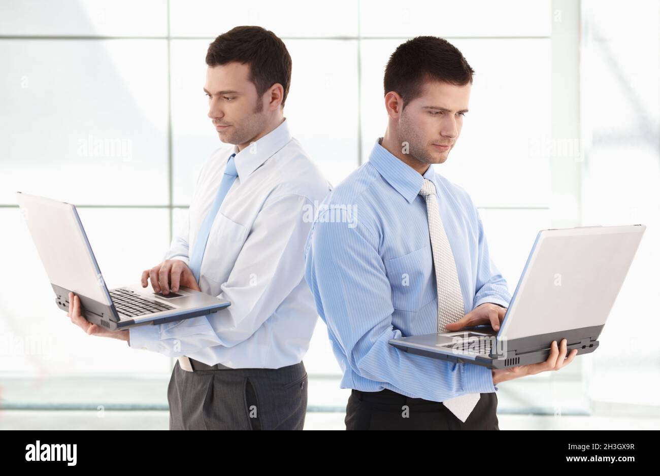 Young businessmen standing with laptop in hands Stock Photo