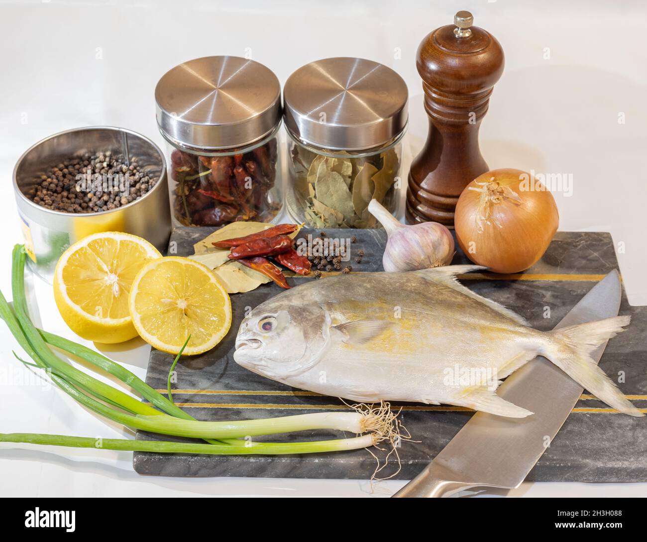 Food background. Fresh, raw fish with a garlic, onion, lemon, and spices on a light background. Preparing for cooking a pompano fish. Selective focus, Stock Photo