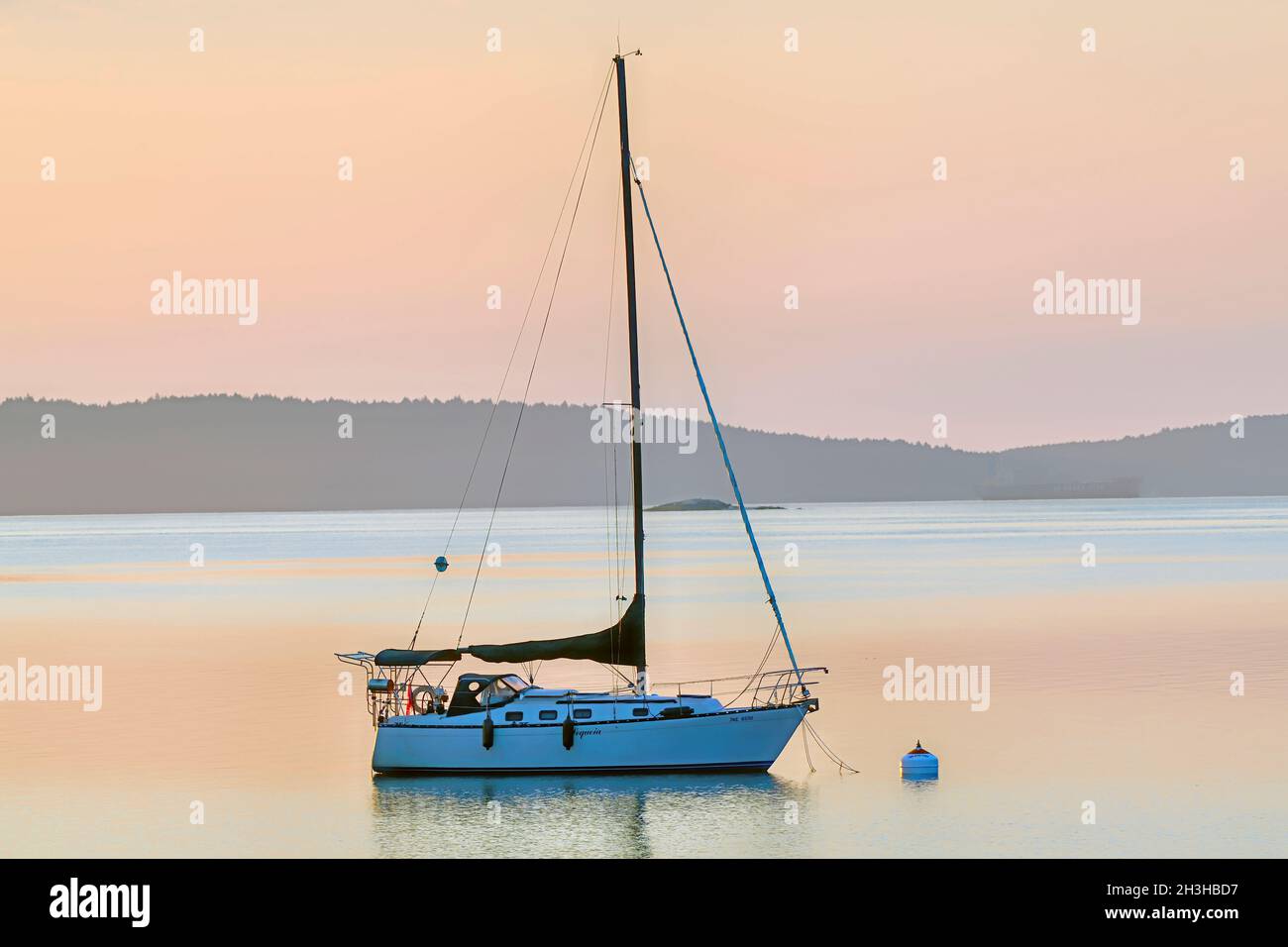 A sail boat moored in the calm water of a secluded bay in the early morning light on Vancouver Island British Columbia Canada. Stock Photo