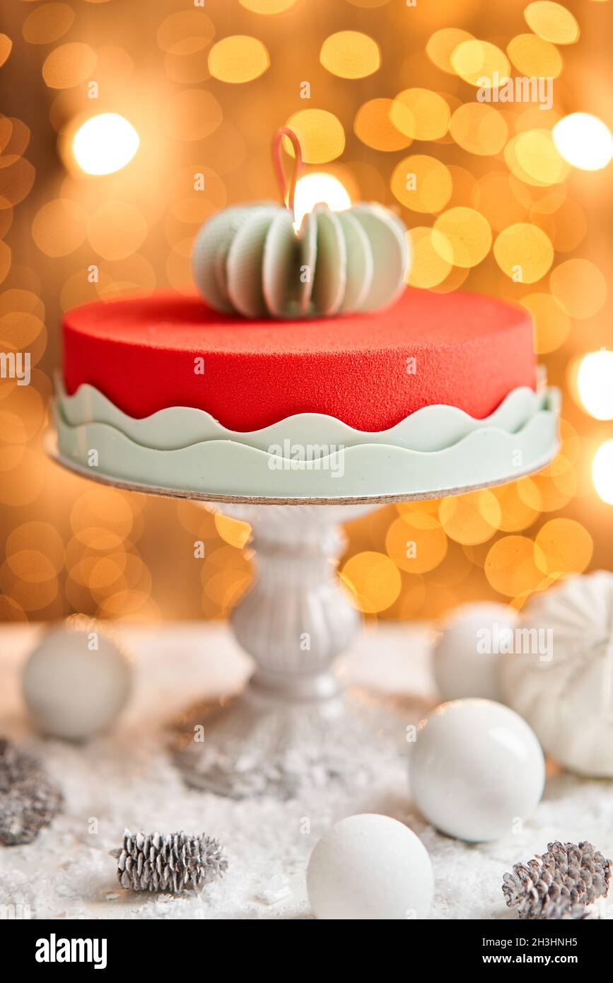 Mousse cake covered with red velour. Garland lamps bokeh on background. Modern european cake. French cuisine. Christmas theme. Copy space Stock Photo