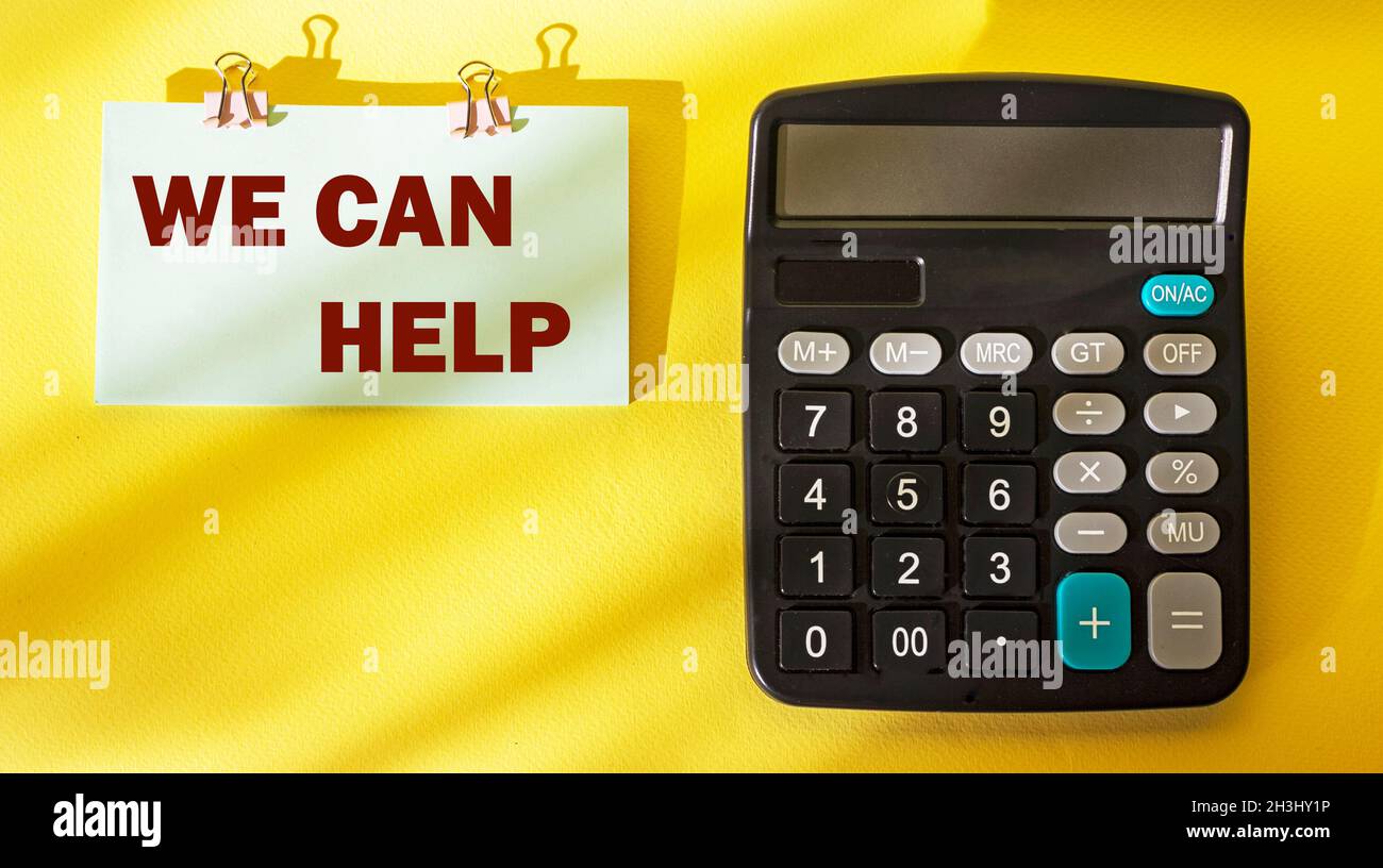 We can help text on a sticker and a yellow background, there is a calculator next to it Stock Photo