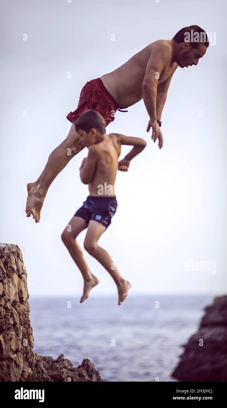 Menorca, Spain - September 8: Man and kid jumping from cliff into sea, on September 8, 2014 Island of Menorca, Balearic Islands, Stock Photo