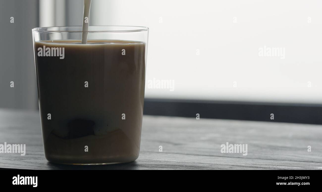 pour milk into ice coffee on black wood table, wide photo Stock Photo