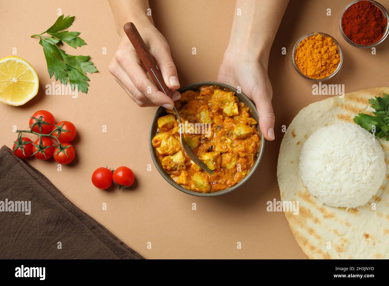 Female hands hold fork and bowl with chicken tikka on beige background Stock Photo